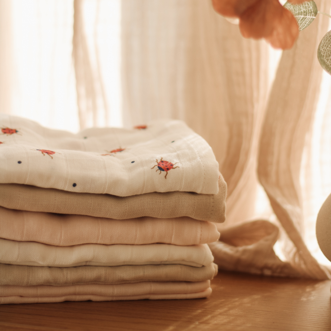 Stack of folded fabric swaddles with embroidered designs on a wooden surface.
