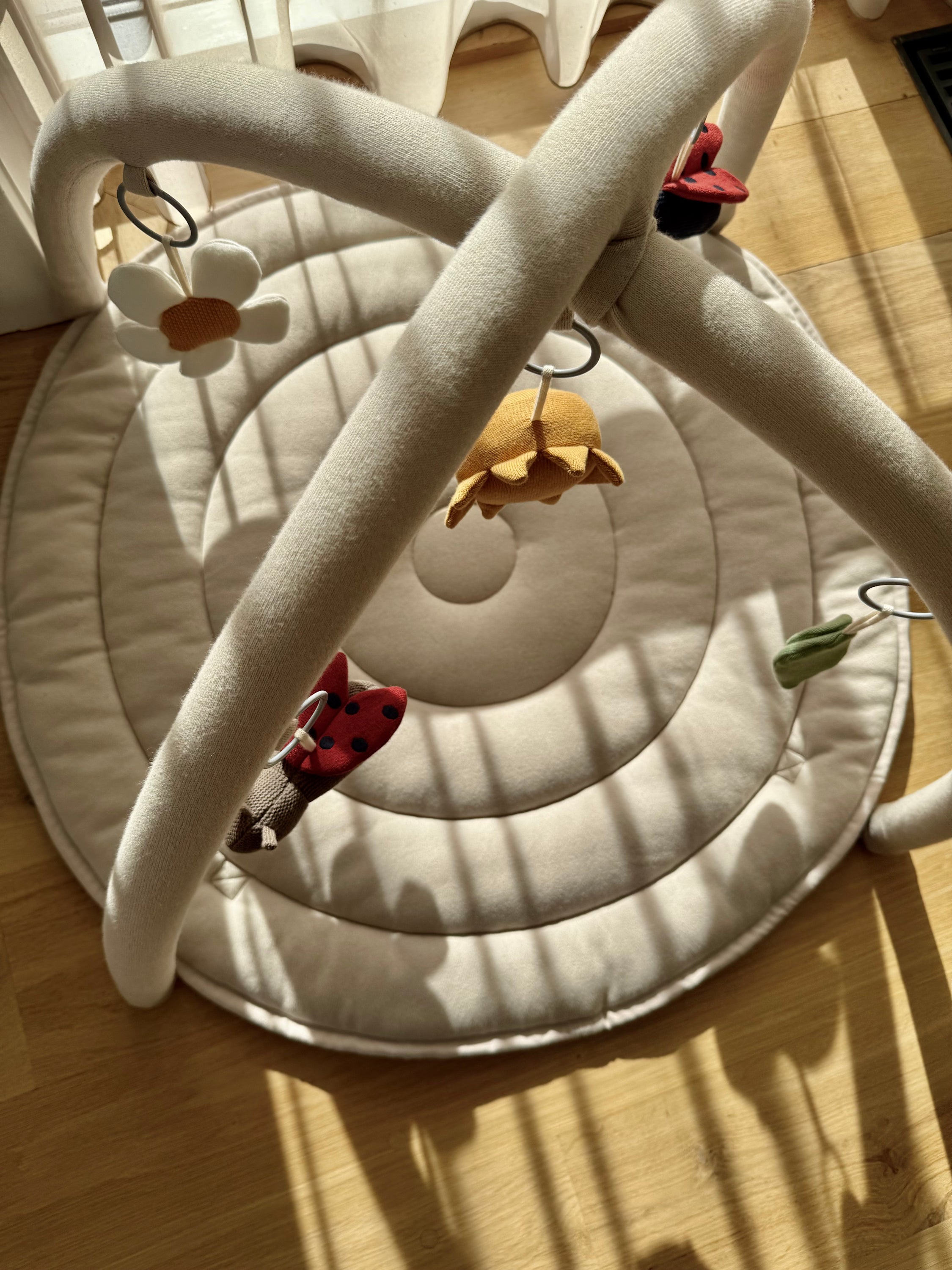 Baby play mat with circular design and hanging toys on a wooden floor